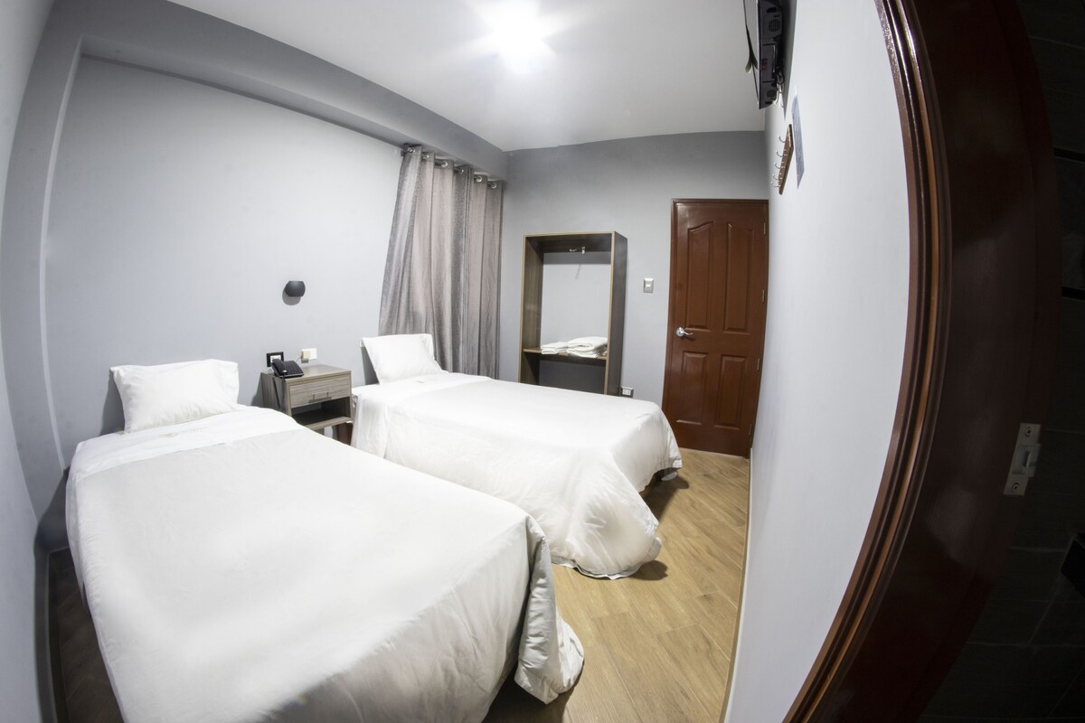 A hotel room with two beds, a wooden door, a wardrobe, and a mirror.