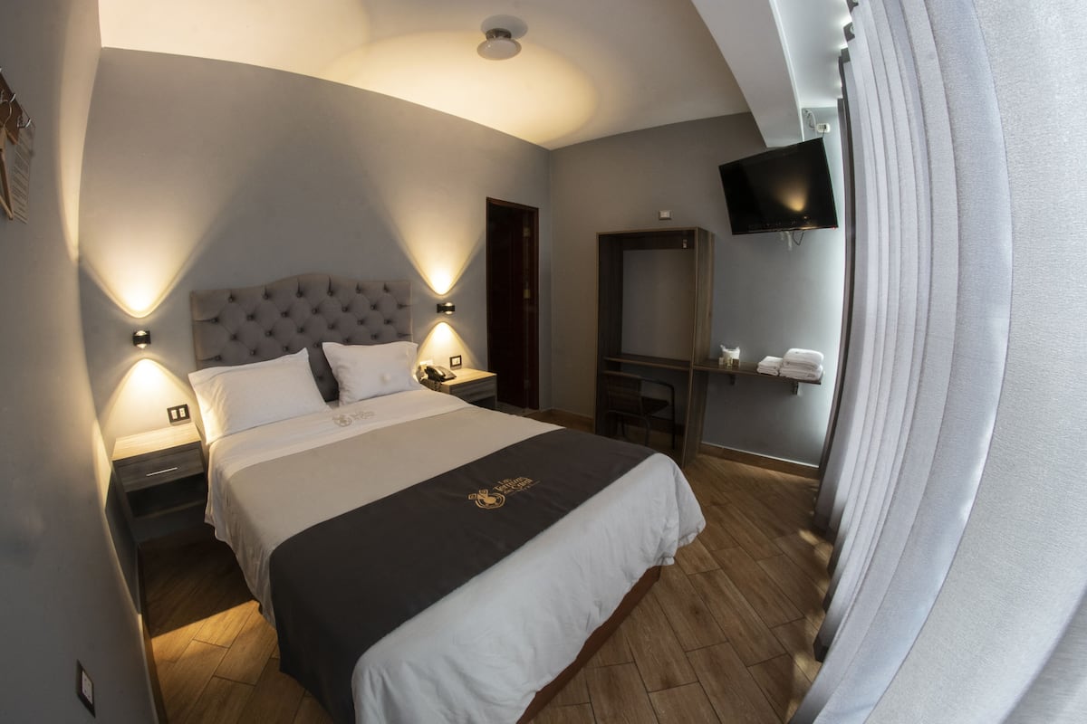 A hotel room with a large bed, bedside lamps, a flat-screen TV, a mirror, and a wooden floor.