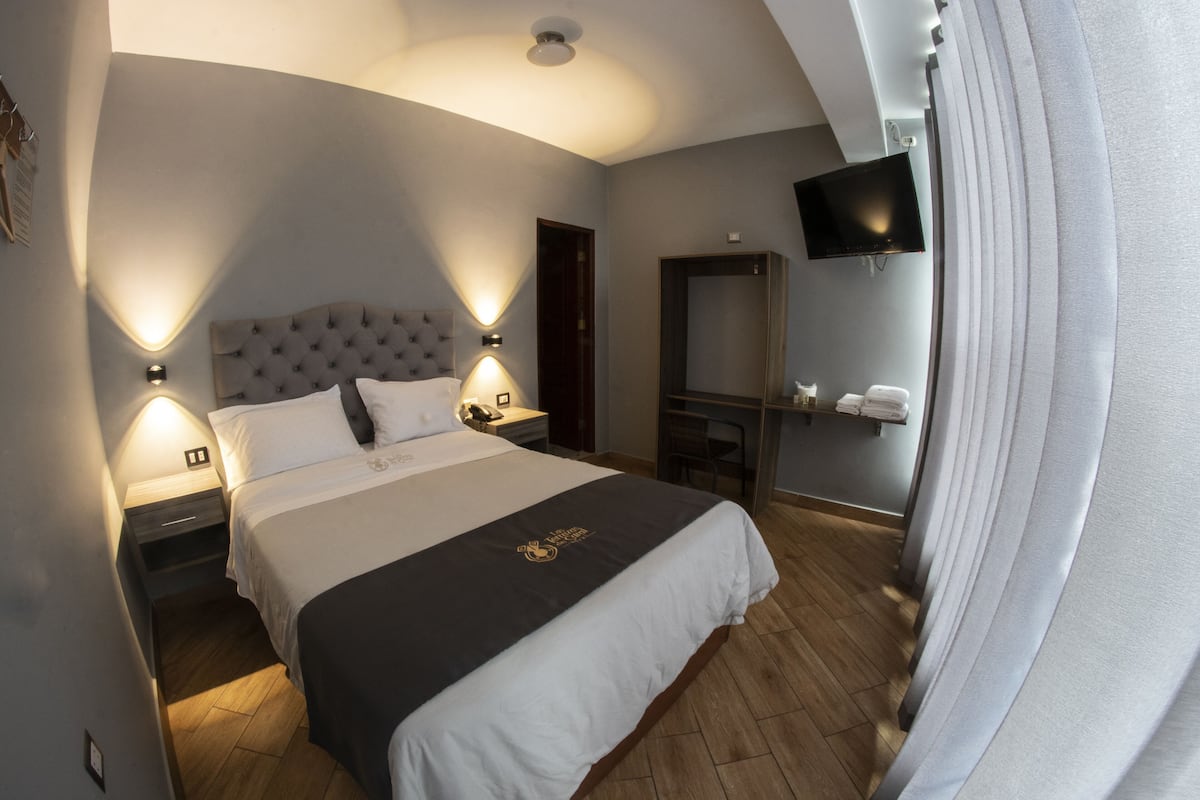 A hotel room with a large bed, two bedside tables, a flat-screen TV mounted on the wall, and a wooden floor.