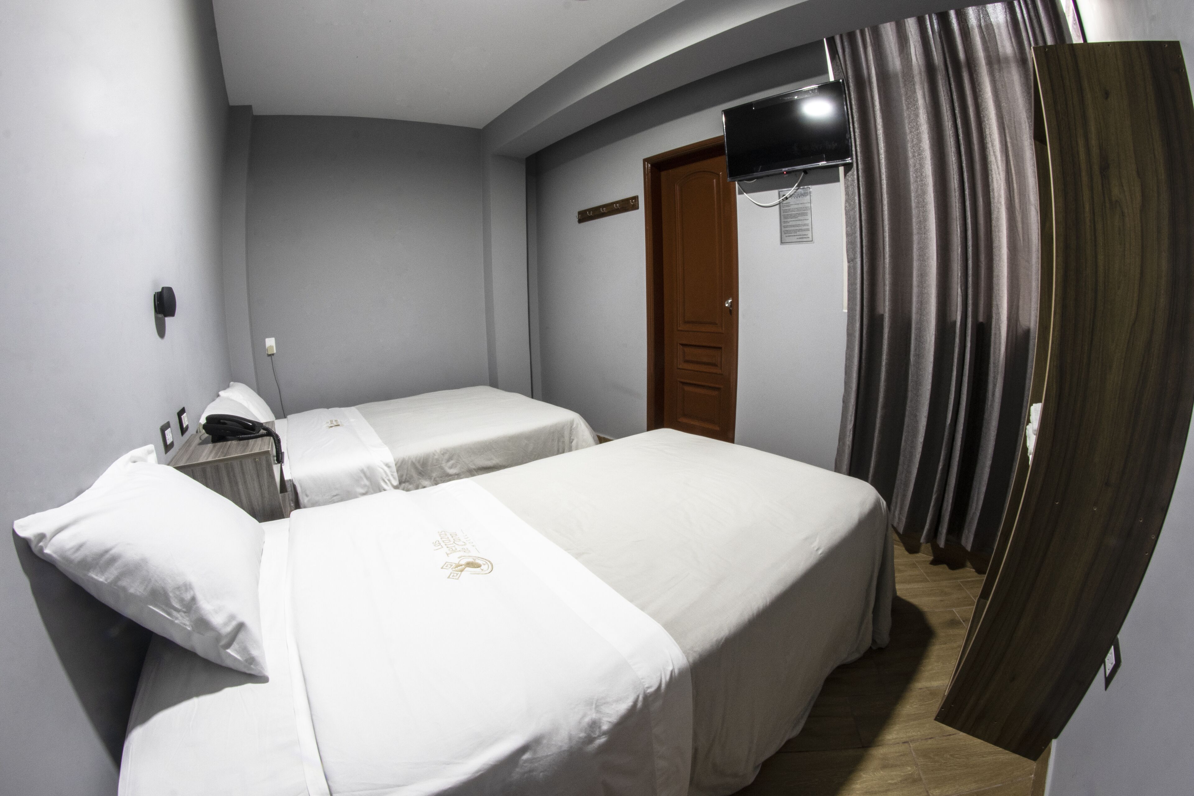 Een hotelkamer met twee eenpersoonsbedden, een wandgemonteerde flatscreen-tv en een houten deur.