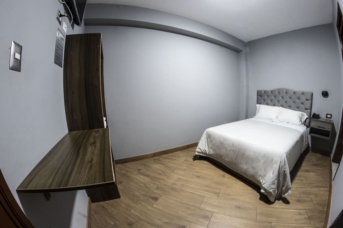 A bedroom with a bed, a nightstand, a wooden desk, and a curved wall.