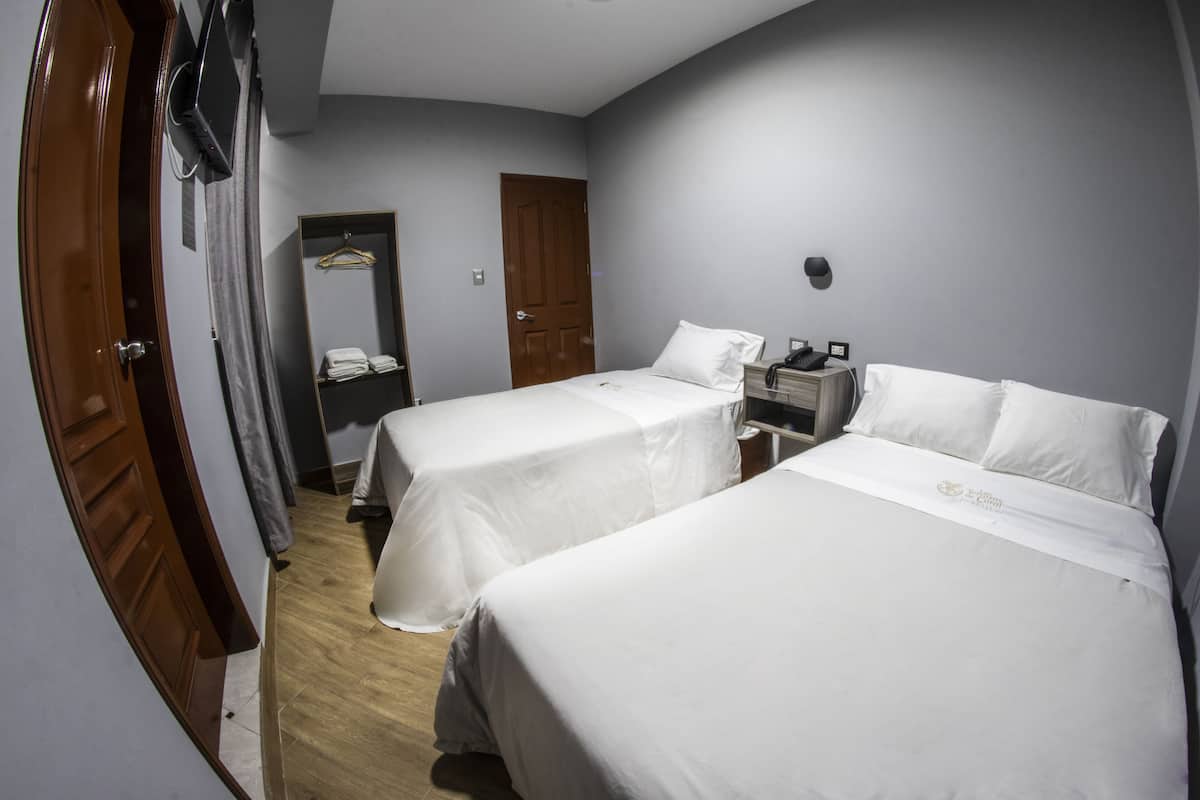 A hotel room with two beds, a wardrobe, a mirror, and a bedside table with a lamp.