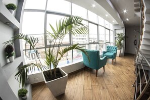 A modern hotel room with large windows, wooden flooring, and teal chairs. - Hotel Las Terrazas de Caral (Barranca)