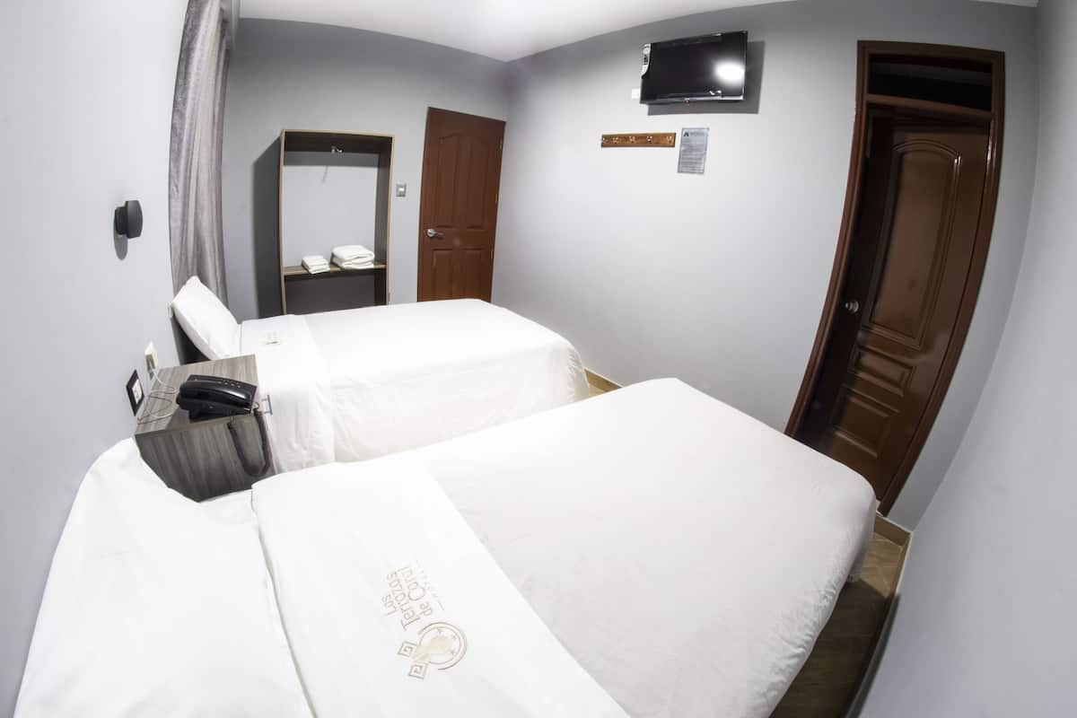 A hotel room with two beds, a desk, a telephone, and a television on the wall.