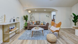 Una sala de estar moderna con un sofá, una mesa de centro y un sillón. Se observa una consola decorada con objetos y una planta en maceta.