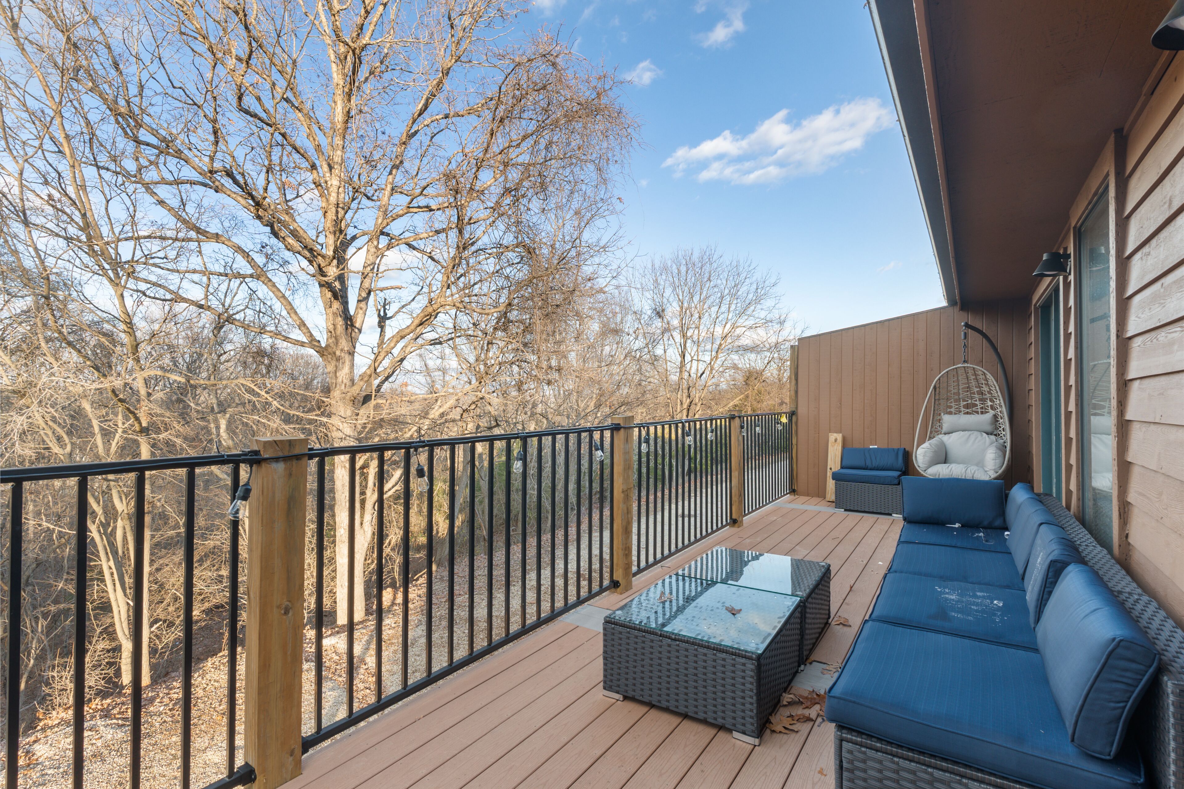 A deck with a blue sofa, a wicker table, and a hanging chair.