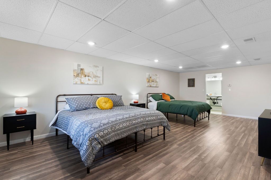 A bedroom with two beds, a nightstand with a lamp, and artwork on the wall.