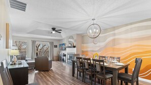 A spacious dining area with a wooden table set for six, a ceiling fan, and a wall mural. - Cozy Modern Branson Game House | 9 Min to SDC (Branson West)