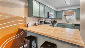 A modern kitchen with green cabinets, a wooden countertop, and two barstools. - Cozy Modern Branson Game House | 9 Min to SDC (Branson West)