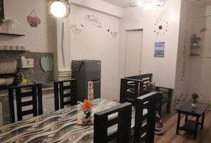 A modern kitchen with white brick walls, a marble countertop, and black chairs around a central dining table with a vase of flowers.