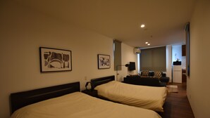 A hotel room with two beds, a desk, a chair, and a small kitchenette. - PrimeRoomBeppu TATAMIsuite (Beppu)