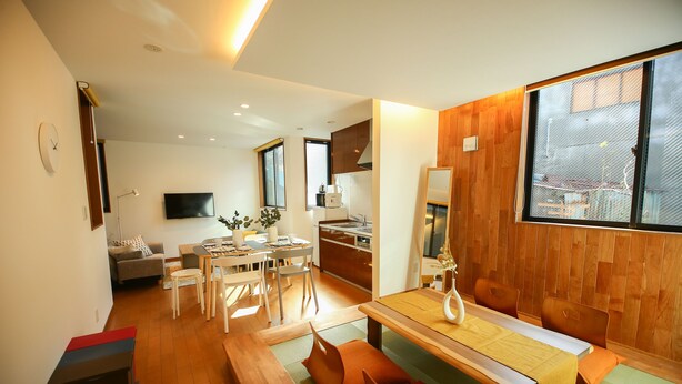 A modern living space with a dining area, kitchen, and a TV mounted on the wall. - PrimeRoomBeppu TATAMIsuite (Beppu)