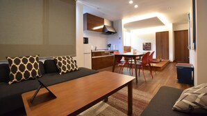 A modern living room with a sofa, a coffee table, and a dining area with chairs and a table. - PrimeRoomBeppu TATAMIsuite (Beppu)