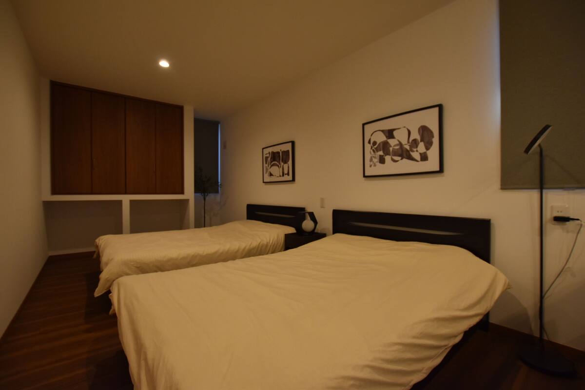 A room with two beds, a wardrobe, and two framed pictures on the wall.
