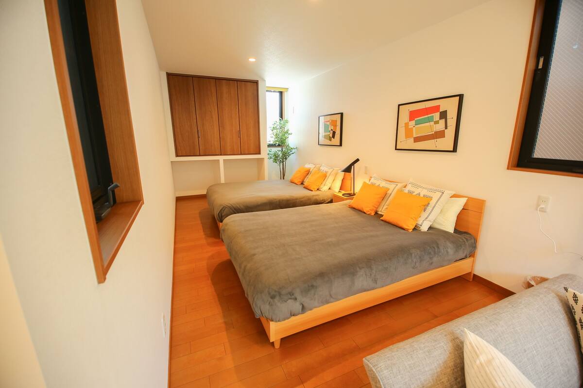 A modern bedroom with two beds, wooden flooring, and a large window.
