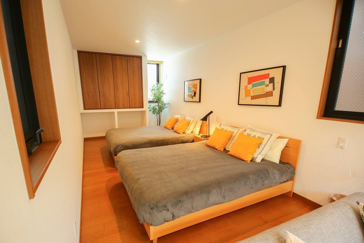 A bedroom with two beds, wooden flooring, a window, and a plant.