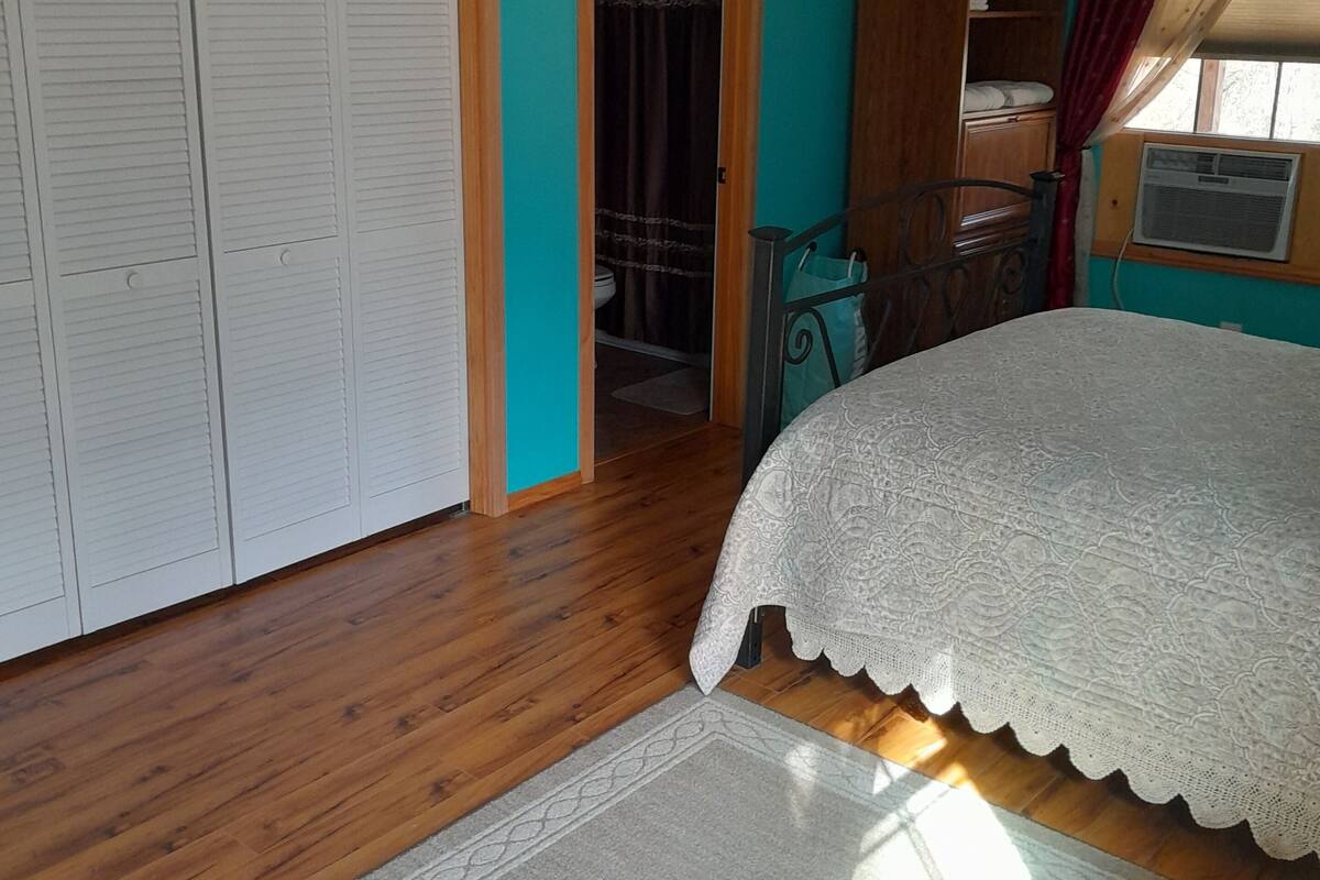 Um quarto com cama, guarda-roupa, porta para um banheiro e janela com cortinas.