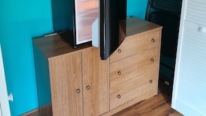 Een kleine kamer met een houten dressoir, een witte kledingkast, en een bed met een wit kussen.