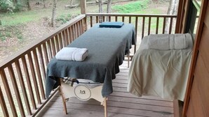 Een houten terras met twee massagetafels, een stoel en een mand.
