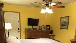 Een slaapkamer met een houten bed, een plafondventilator, een dressoir en een televisie aan de muur.