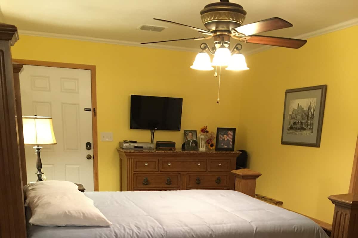 Quarto com cama de madeira, ventoinha no teto, cômoda e televisão na parede.