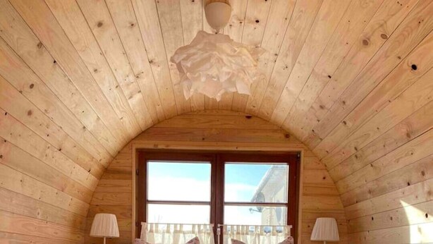 Camera da letto accogliente in legno con soffitto spiovente, due letti con biancheria da letto floreale, una finestra e due lampade da comodino.