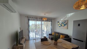 Een moderne woonkamer met een bank, eettafel en een groot raam met gordijnen.