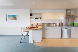 A modern kitchen with white cabinets, a stainless steel dishwasher, and a wooden island with bar stools.