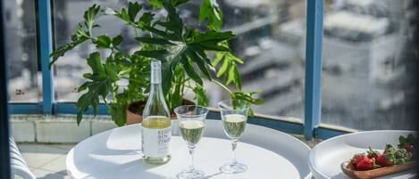 A table with a bottle and two glasses of white wine, a plate with strawberries, and a large green plant in the background.