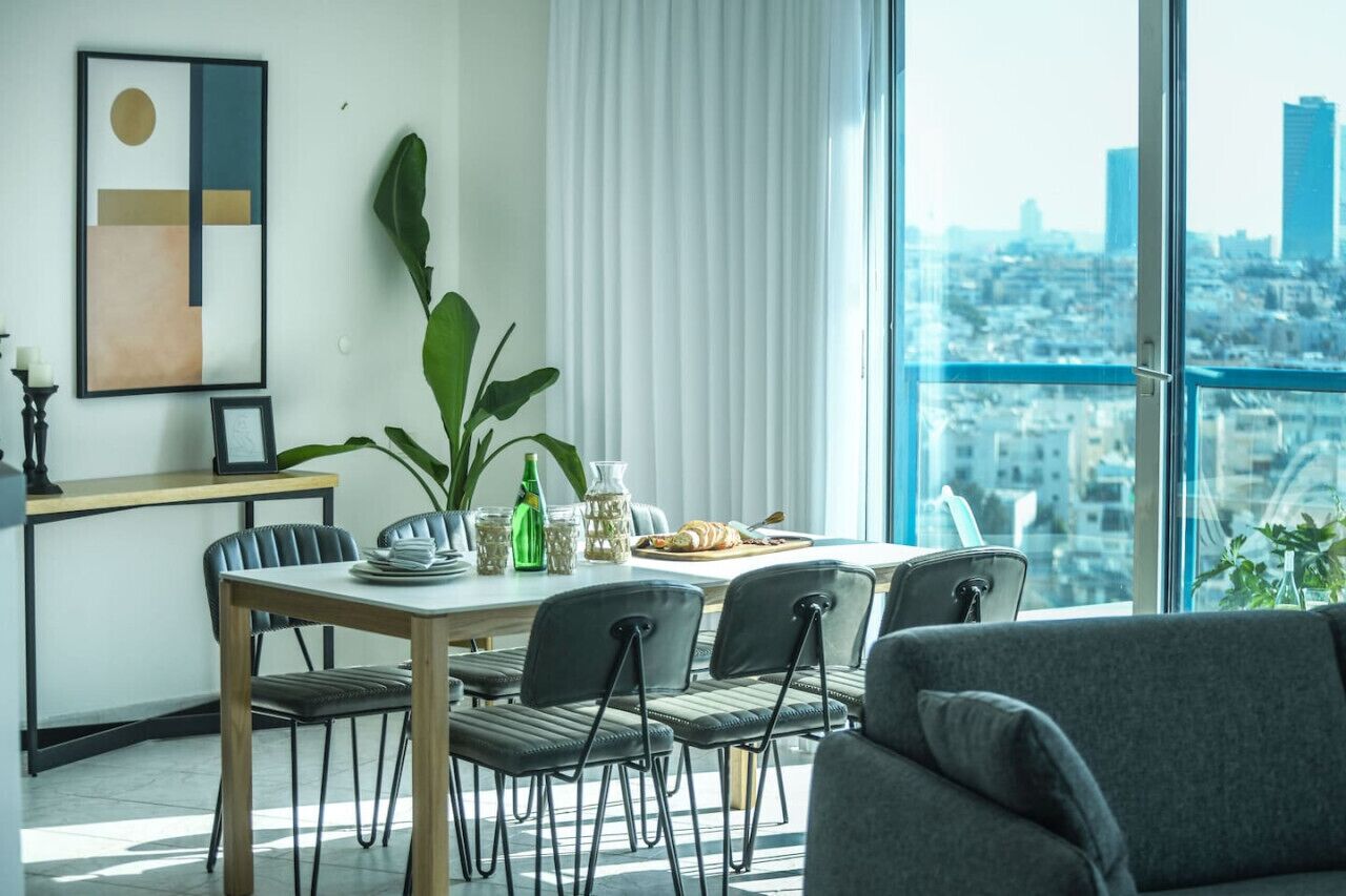 Un comedor moderno con vistas a la ciudad, una mesa dispuesta con platos, una botella y un croissant.