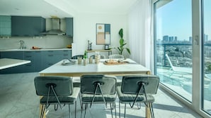 Una cocina moderna con armarios grises, una isla grande y un comedor con cuatro sillas. Hay una ventana grande con vista a la ciudad.