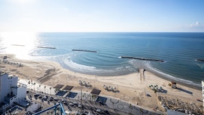 Vista costera con playa, océano y una carretera con vehículos y edificios.