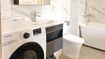 A modern bathroom with a washing machine, a sink, a toilet, and a bathtub.