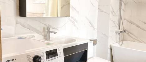A modern bathroom with a washing machine, a sink, a toilet, and a bathtub.
