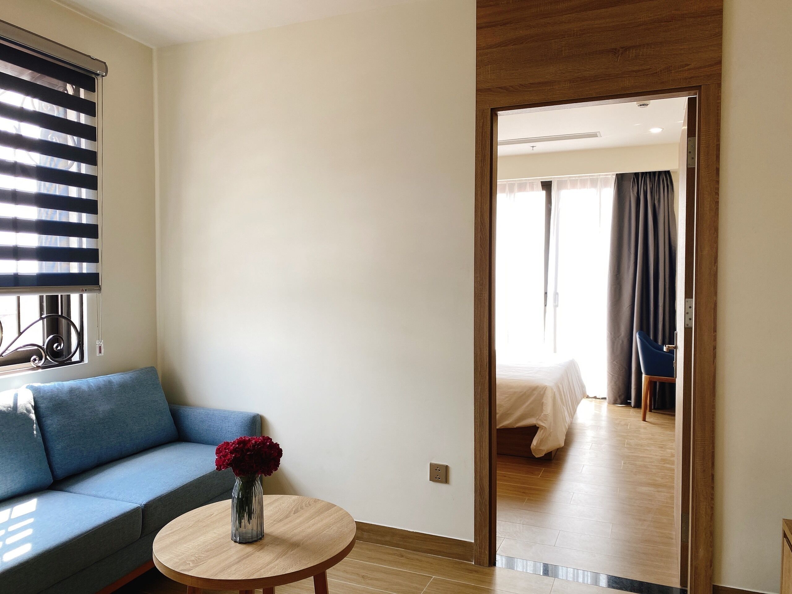A hotel room with a sofa, a small round table with a vase of flowers, and a view into the adjacent bedroom.