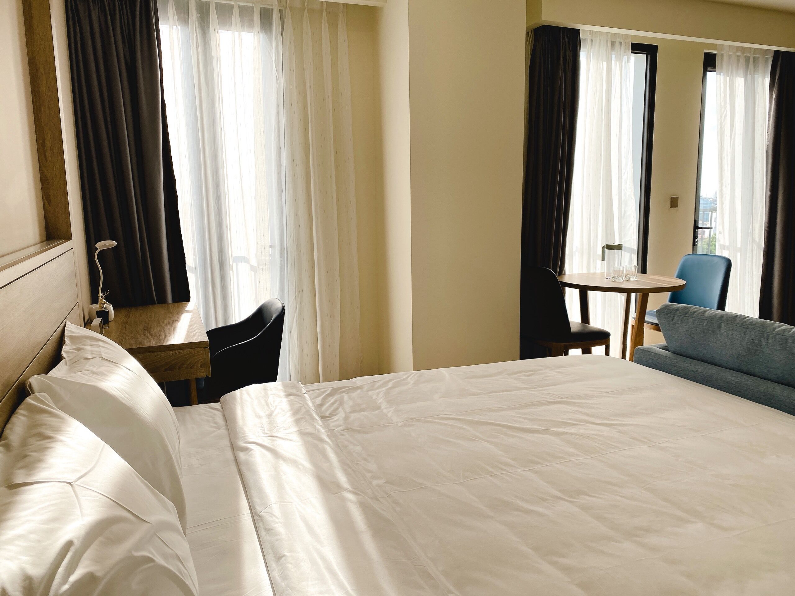 A hotel room with a large bed, a desk, a chair, a sofa, and a small table with glasses.