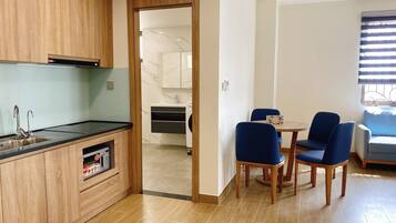 A modern kitchen with wooden cabinets, a built-in microwave, and a sink. There is a dining area with two blue chairs and a small table.