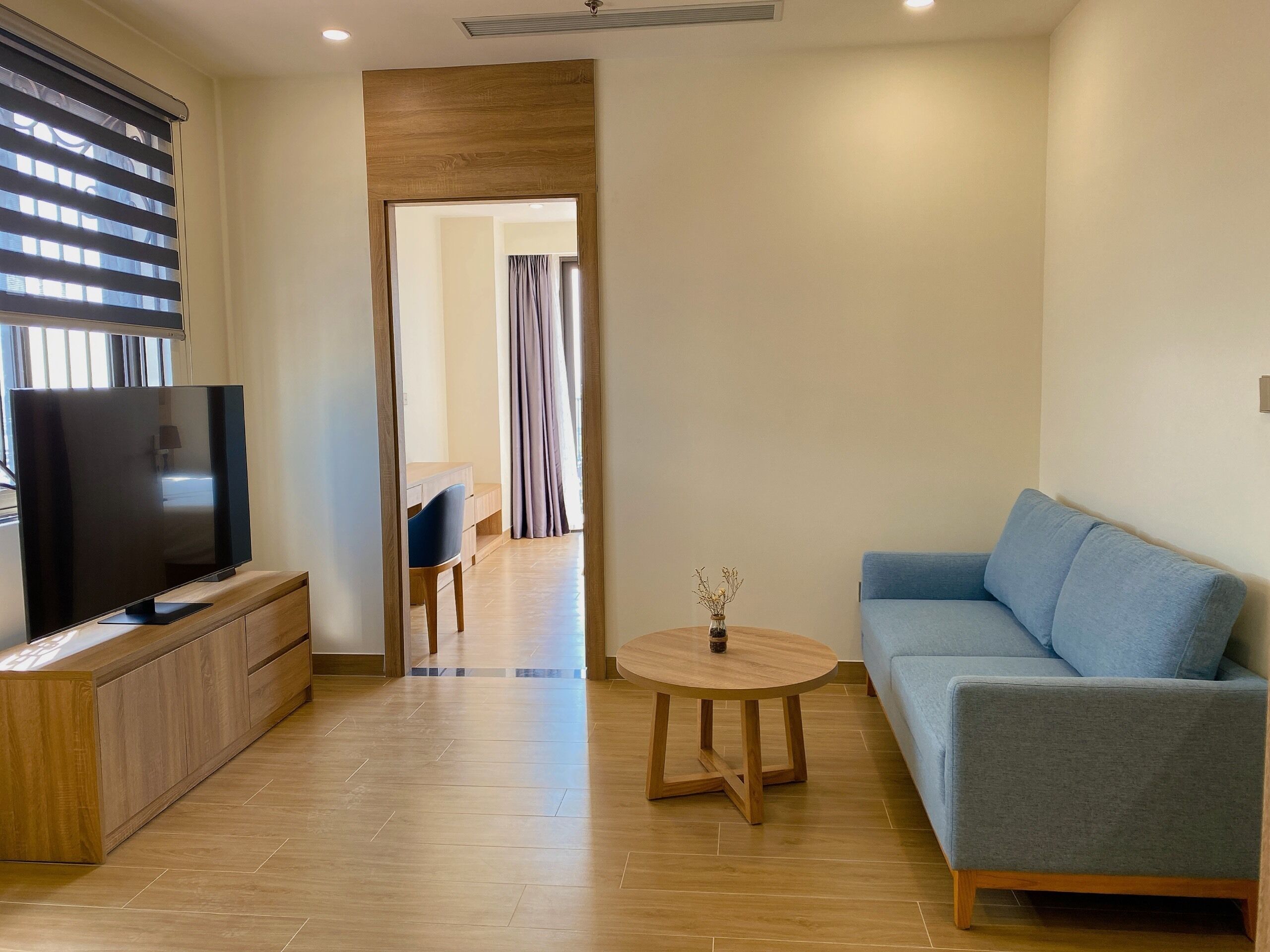 A modern living room with a flat-screen TV, a blue sofa, a wooden coffee table, and a wooden cabinet.