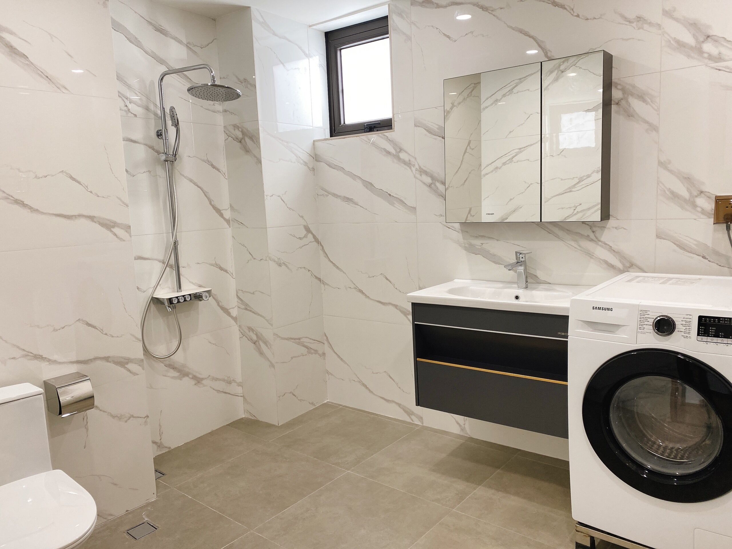A modern bathroom with a marble backsplash, a built-in shower, a sink with a mirror above, and a front-loading washing machine.
