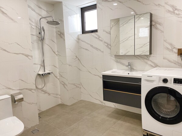 Un baño moderno con salpicadero de mármol, ducha integrada, lavabo con espejo superior y lavadora de carga frontal.