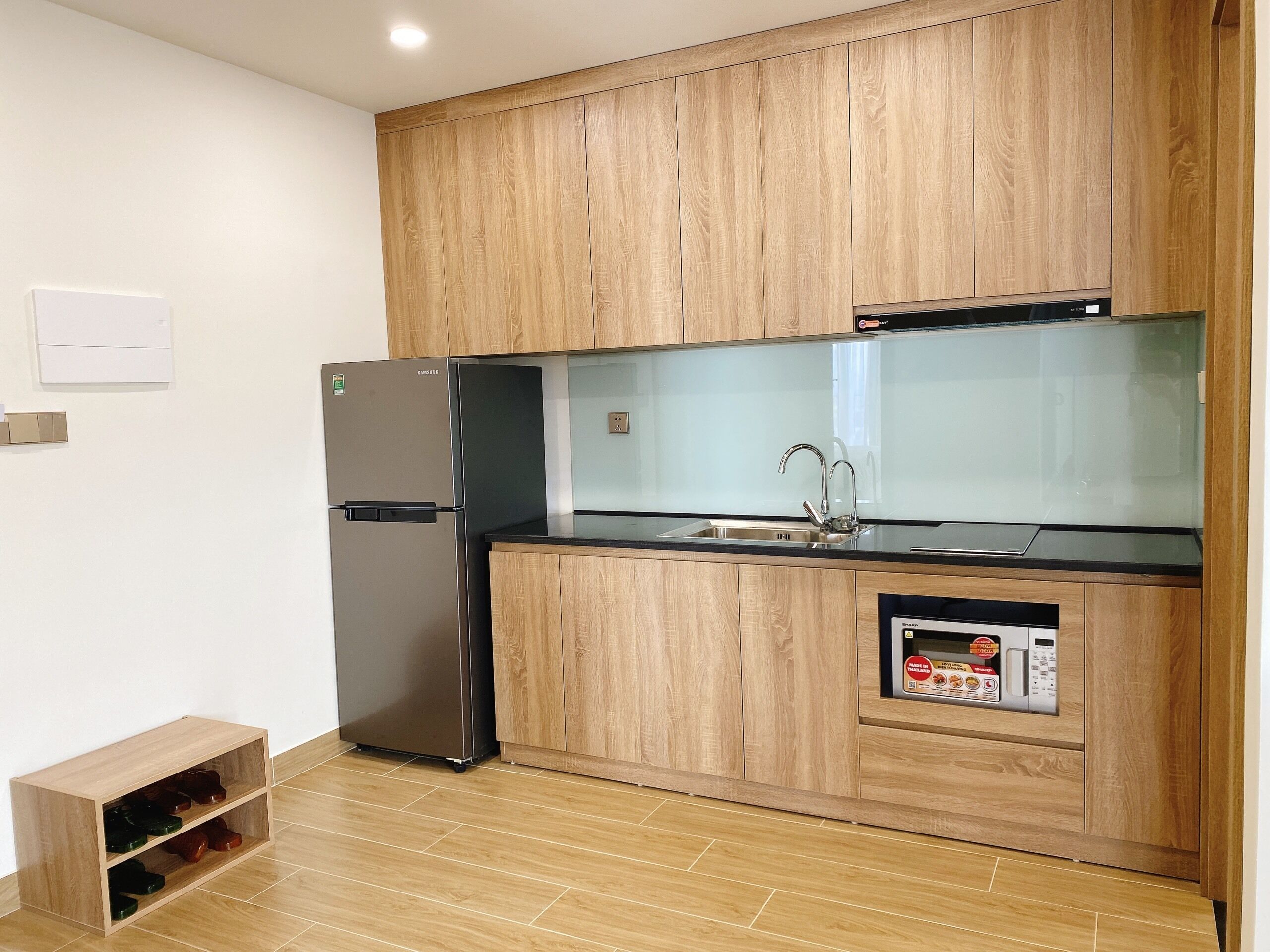 A compact kitchen with wooden cabinets, a stainless steel refrigerator, a microwave, and a built-in oven.
