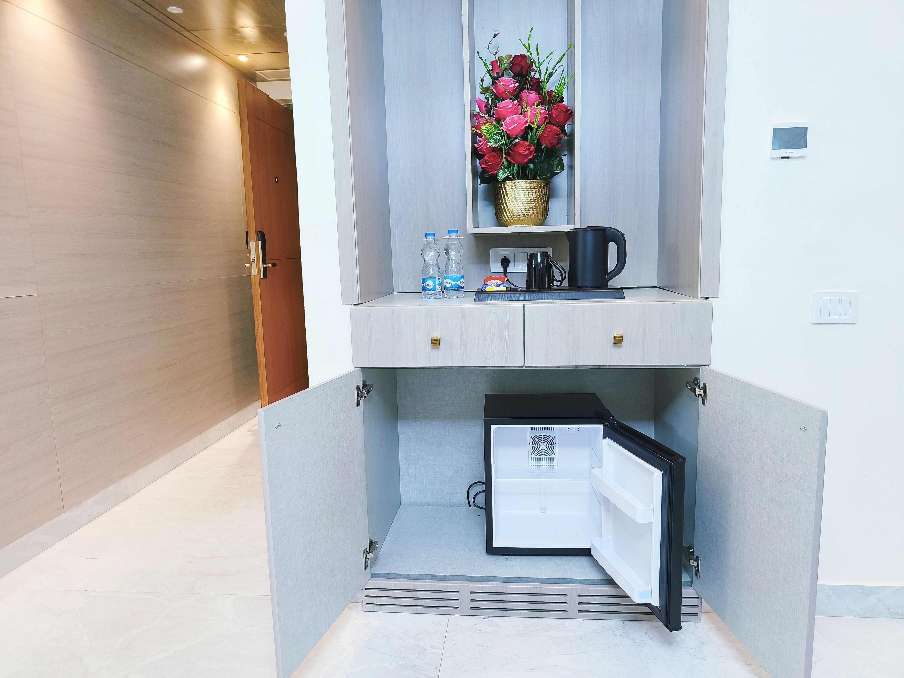 Una kitchenette compacta con refrigerador, cafetera y dispensador de agua.