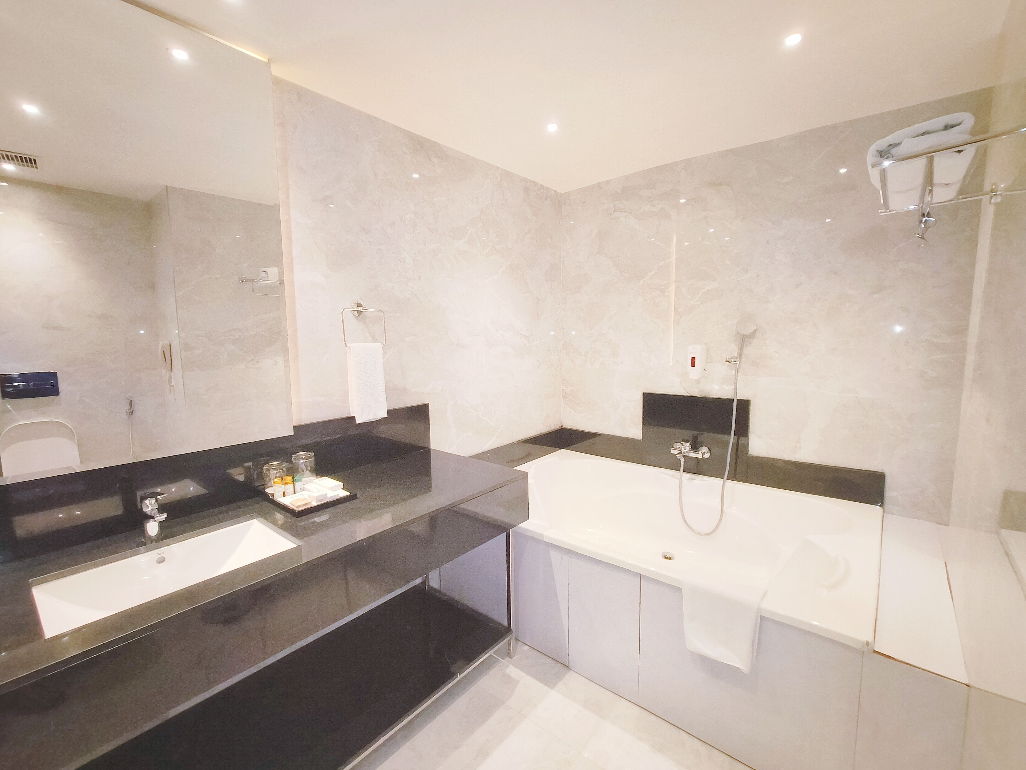 Un bagno moderno con uno specchio grande, una vasca da bagno e un angolo lavabo separato.
