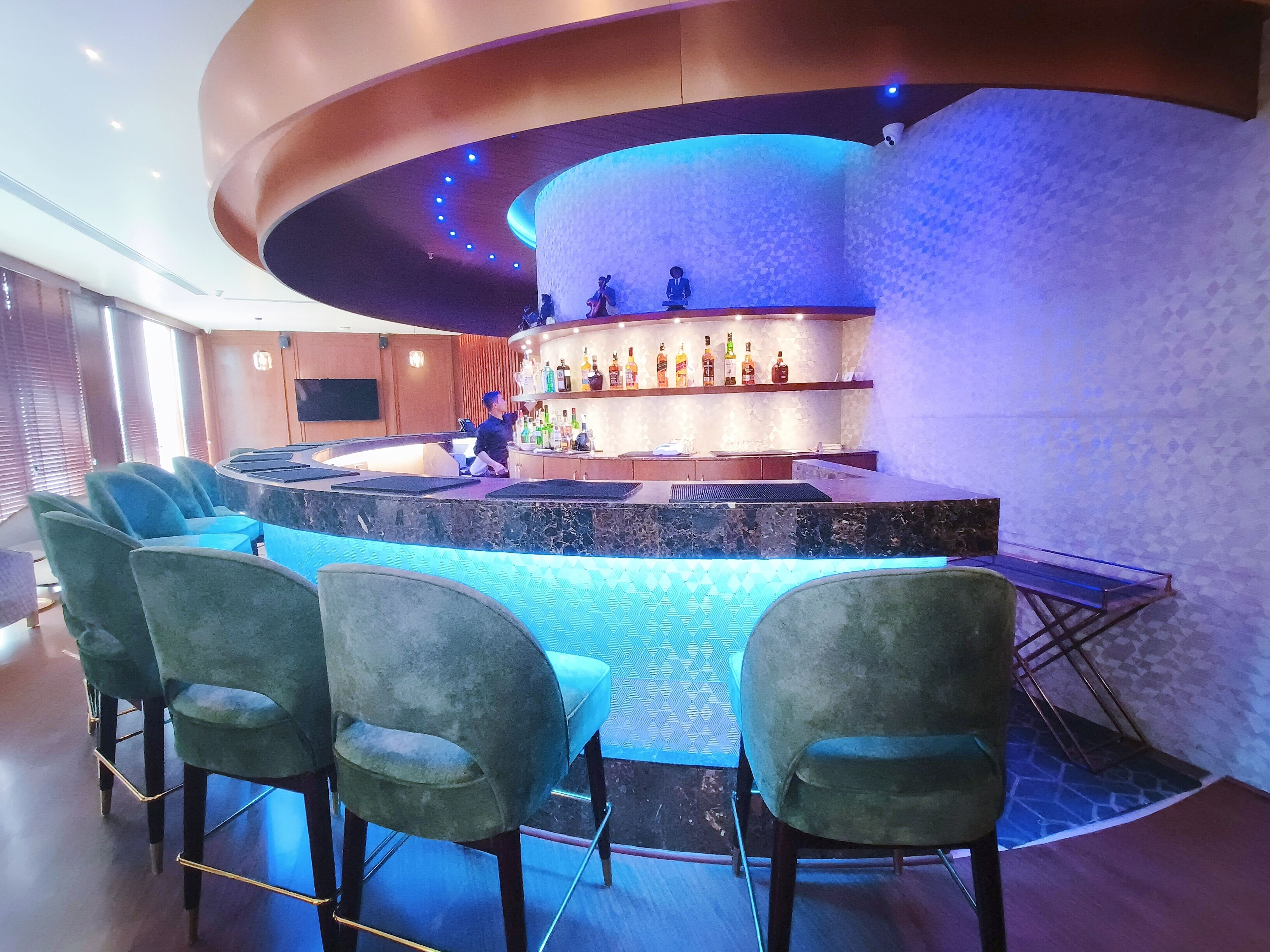 Een bar met een gebogen toonbank, barstoelen en diverse flessen drank.