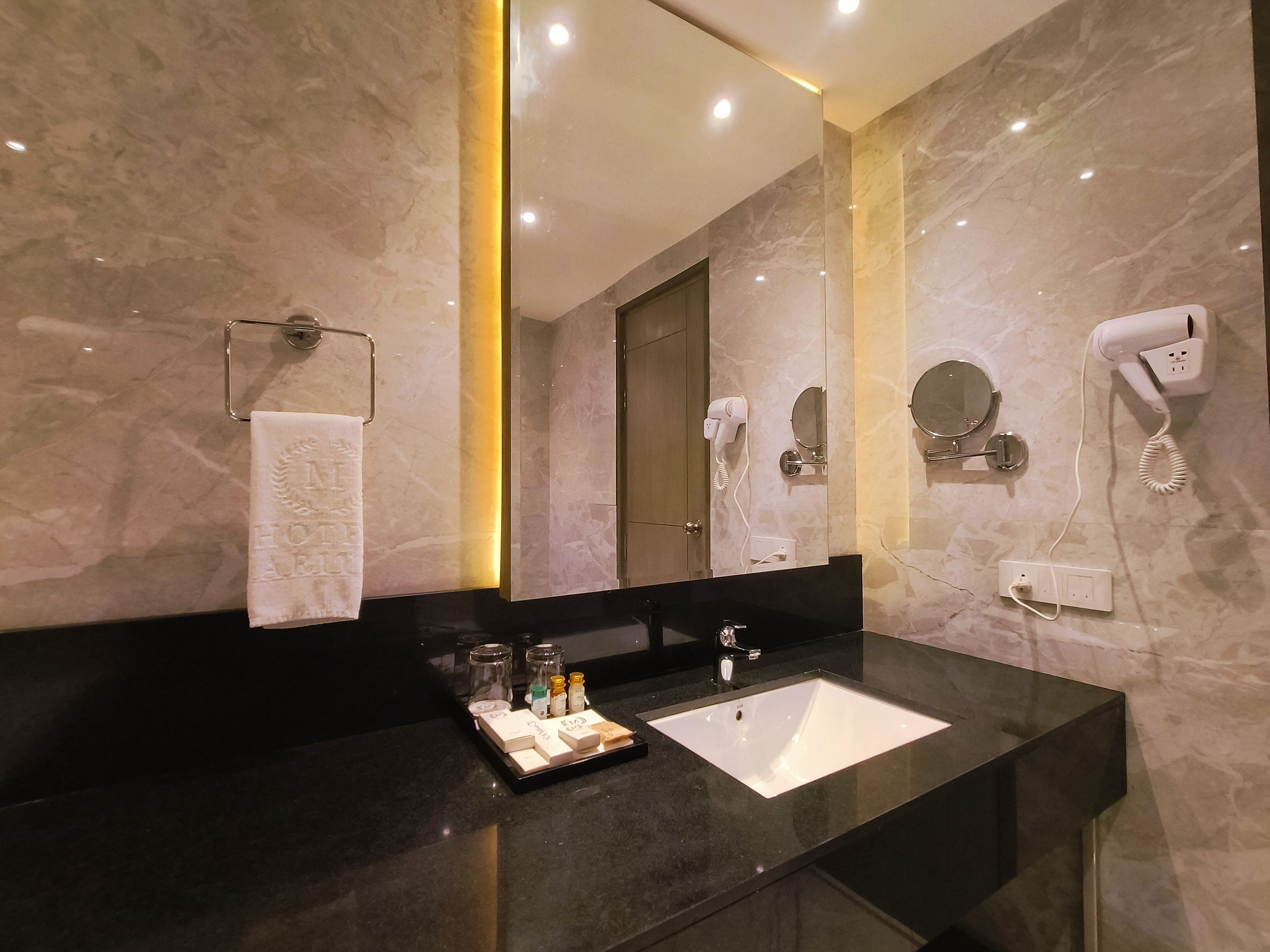 A modern bathroom with a marble vanity, a large mirror, a hairdryer, and a sink.