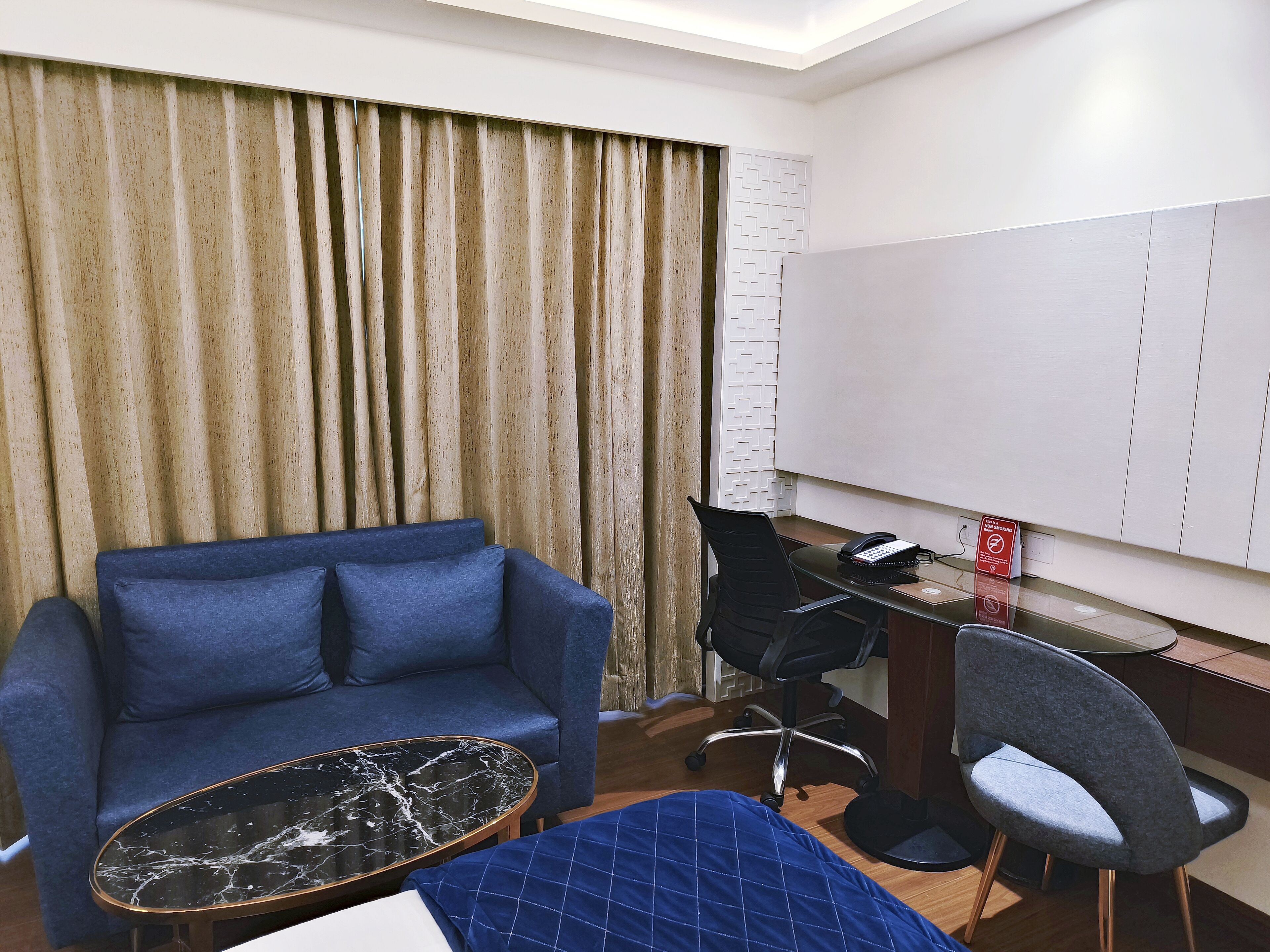 Ein Hotelzimmer mit einem blauen Sofa, einem schwarzen Marmor-Couchtisch, einem Schreibtisch mit Telefon und einem Sessel.