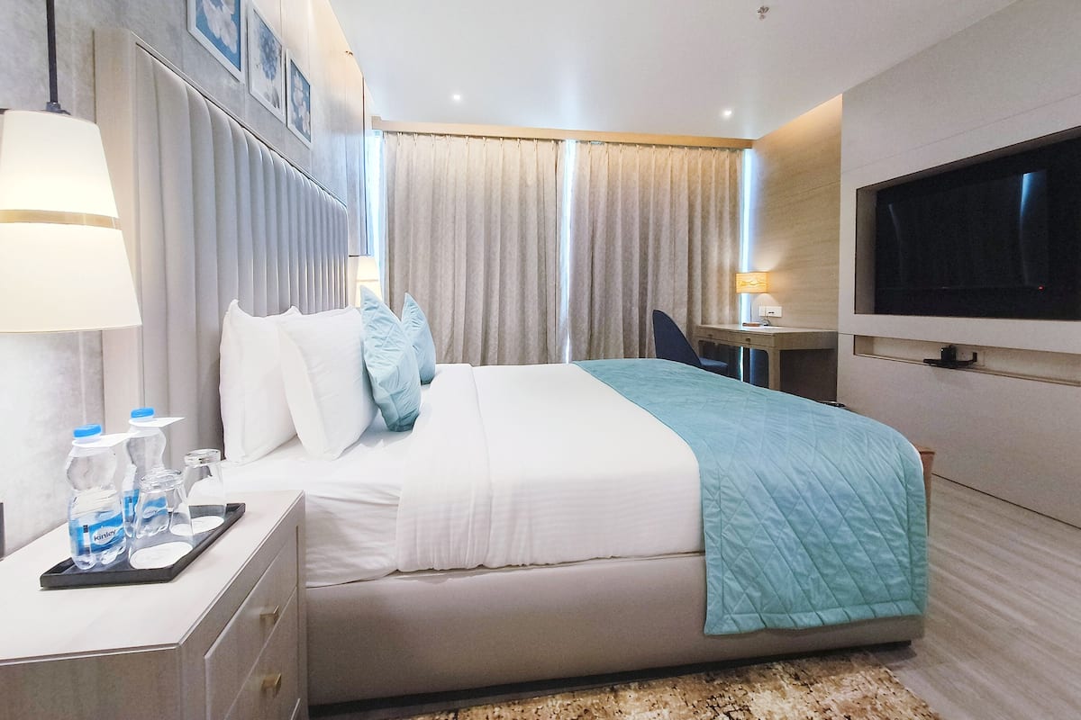 A modern hotel room with a bed, bedside table, TV, and curtains.