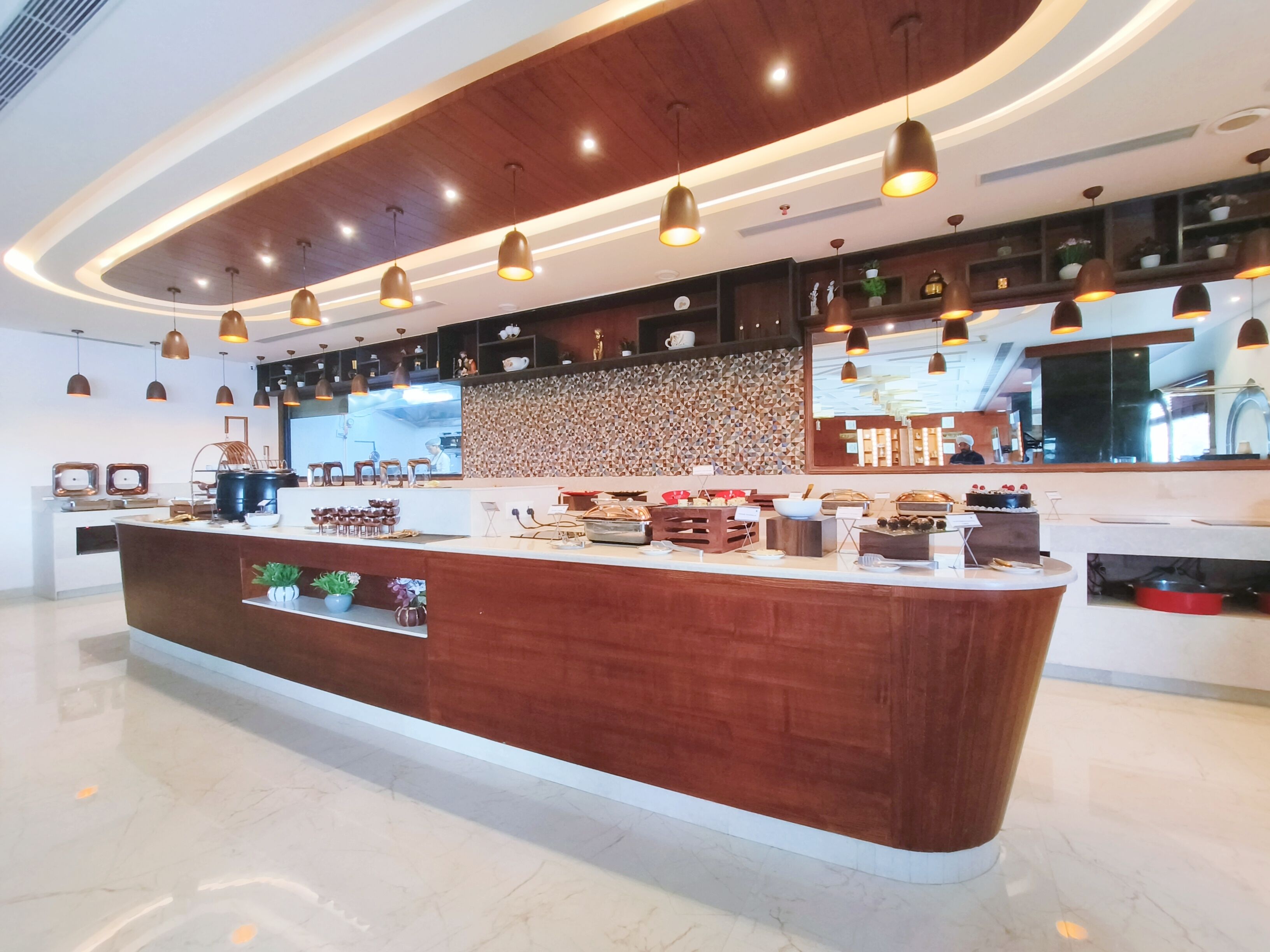 A modern hotel lobby with a central reception desk, pendant lighting, and a decorative wall.