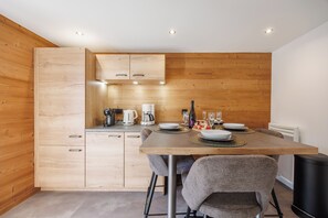 A modern kitchen with wooden cabinets, a dining table set for four, and a coffee maker.