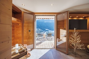 A wooden interior with a glass door leading to a deck with outdoor seating and a snowy mountain view.